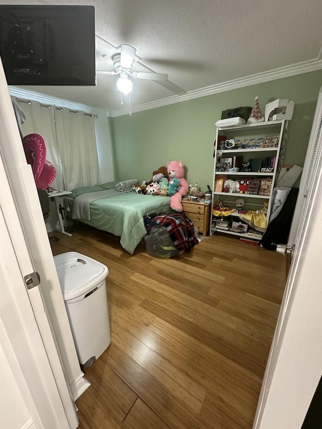 bedroom featuring ceiling fan, hardwood / wood-style flooring, ornamental molding, and a textured ceiling