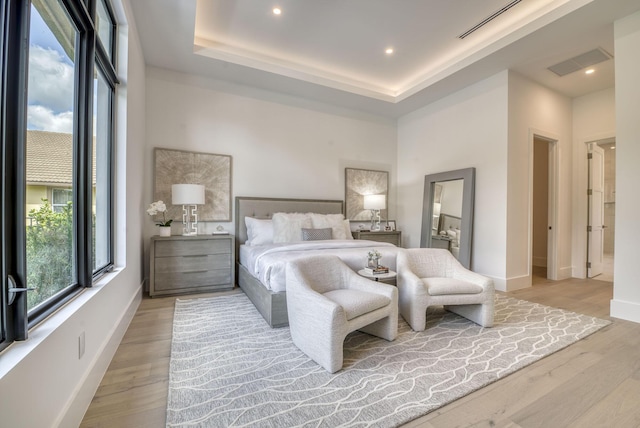 bedroom with light hardwood / wood-style floors and a tray ceiling