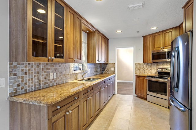 kitchen featuring sink, light tile patterned floors, stainless steel appliances, light stone countertops, and decorative backsplash