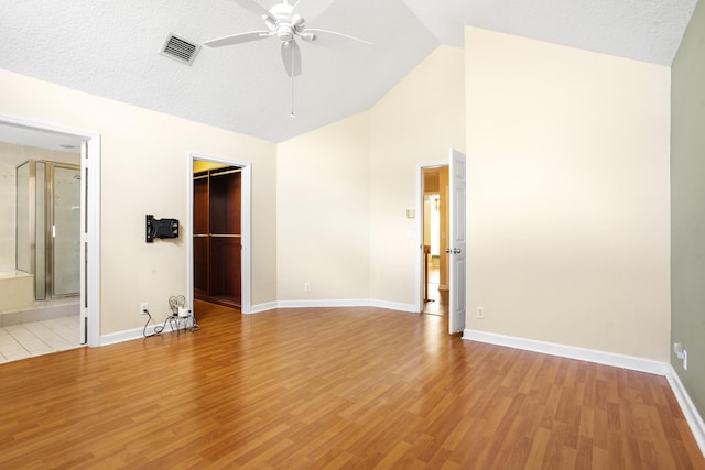 interior space featuring high vaulted ceiling, ensuite bath, light wood-type flooring, a spacious closet, and a textured ceiling