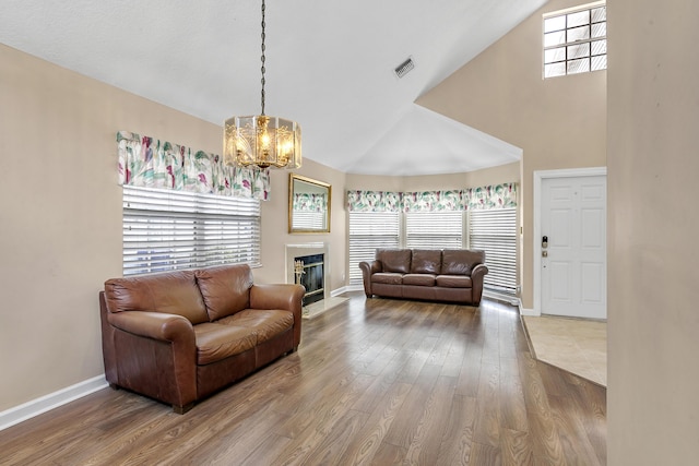 living room with an inviting chandelier, a healthy amount of sunlight, wood-type flooring, and high vaulted ceiling