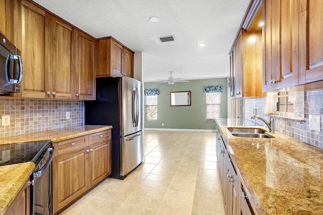 kitchen featuring stainless steel appliances, light stone countertops, sink, and ceiling fan