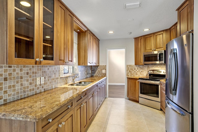 kitchen with light tile patterned flooring, sink, light stone counters, stainless steel appliances, and decorative backsplash