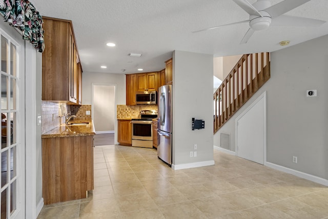 kitchen with sink, ceiling fan, appliances with stainless steel finishes, light stone counters, and decorative backsplash