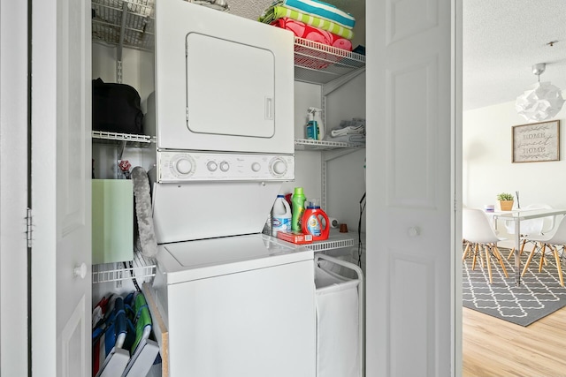 laundry room featuring stacked washer and clothes dryer, a textured ceiling, and light hardwood / wood-style floors