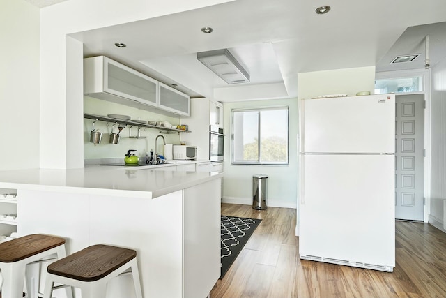 kitchen with a kitchen bar, white cabinetry, light hardwood / wood-style flooring, kitchen peninsula, and white appliances