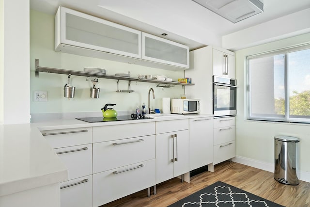 kitchen featuring sink, white cabinetry, light hardwood / wood-style flooring, black electric stovetop, and oven