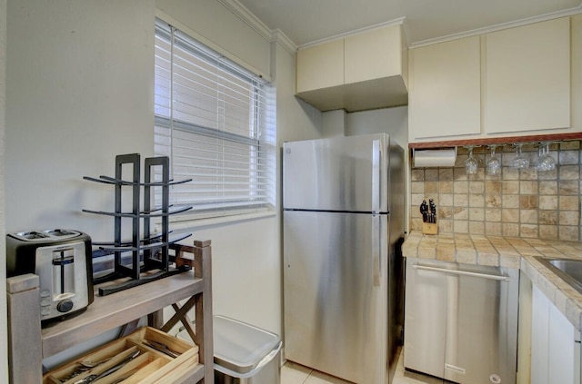 kitchen with appliances with stainless steel finishes, white cabinetry, backsplash, tile counters, and ornamental molding