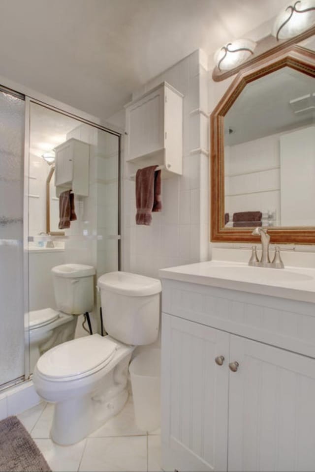 bathroom featuring vanity, a shower with door, tile patterned floors, and toilet