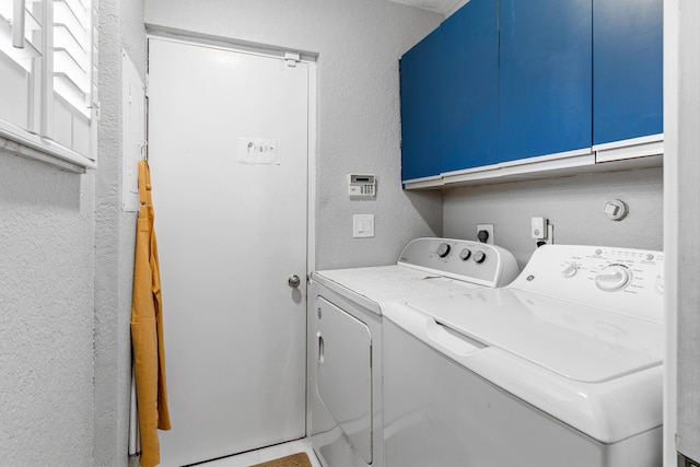 washroom featuring a textured wall, washer and clothes dryer, and cabinet space