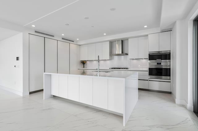 kitchen with a center island with sink, wall chimney exhaust hood, modern cabinets, white cabinetry, and a sink