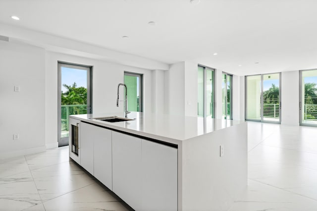 kitchen featuring white cabinets, marble finish floor, a kitchen island with sink, light countertops, and a sink