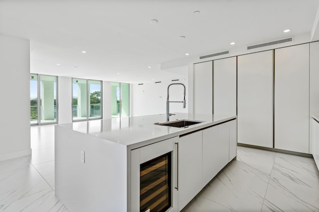 kitchen featuring wine cooler, a kitchen island with sink, a sink, white cabinetry, and marble finish floor