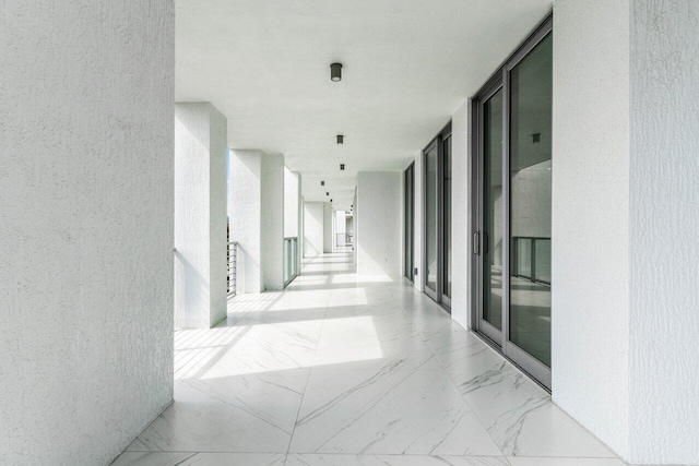 hallway featuring expansive windows, marble finish floor, and a textured wall