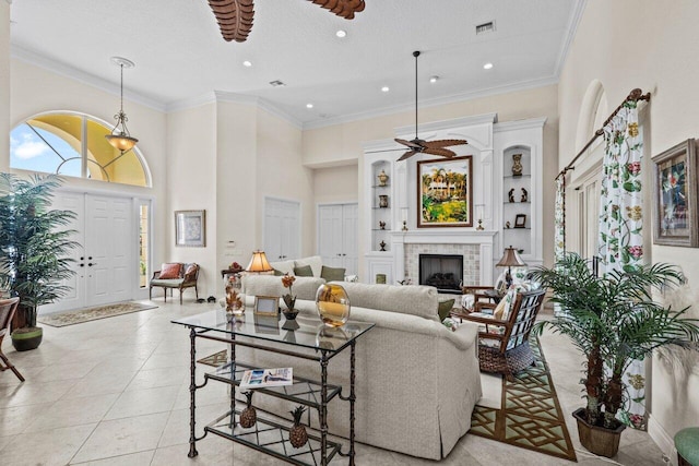 living room featuring light tile patterned floors, crown molding, ceiling fan, a towering ceiling, and a brick fireplace