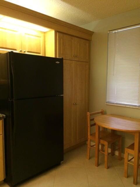 kitchen with black refrigerator, light tile patterned floors, and a textured ceiling