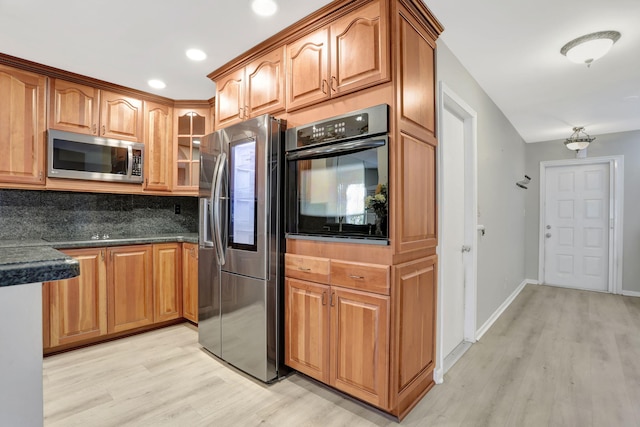 kitchen with decorative backsplash, light hardwood / wood-style floors, dark stone counters, and appliances with stainless steel finishes