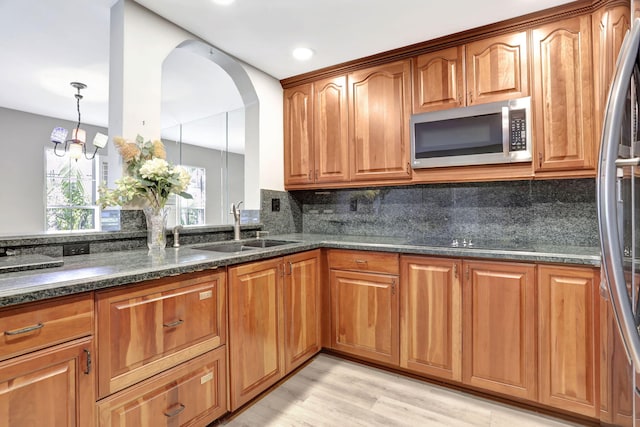 kitchen featuring appliances with stainless steel finishes, decorative light fixtures, sink, dark stone countertops, and backsplash