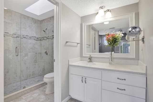 bathroom with toilet, a shower with shower door, a skylight, a textured ceiling, and vanity