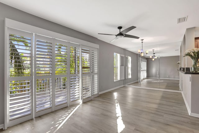 empty room with ceiling fan with notable chandelier and light hardwood / wood-style floors