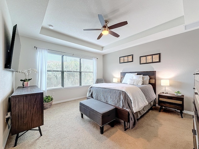 bedroom with light carpet, ceiling fan, a raised ceiling, and a textured ceiling