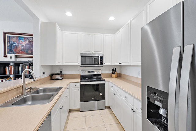 kitchen with light tile patterned floors, appliances with stainless steel finishes, white cabinets, and a sink