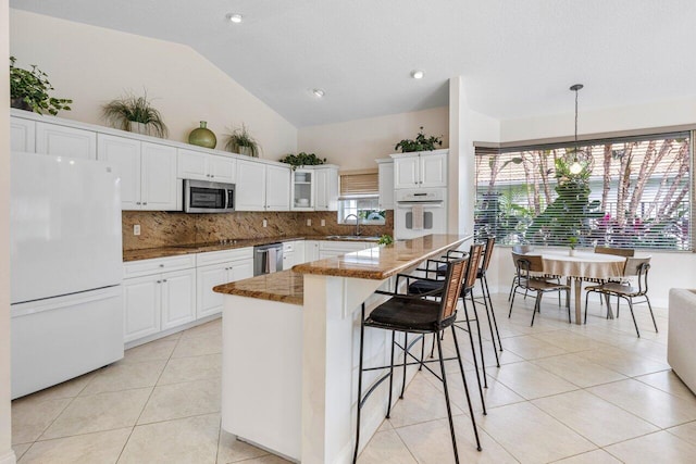 kitchen with white appliances, tasteful backsplash, light tile patterned floors, white cabinetry, and a sink