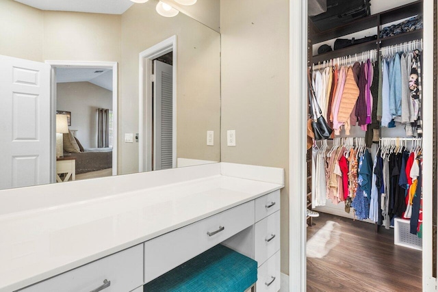 bathroom with visible vents, wood finished floors, vaulted ceiling, a walk in closet, and vanity