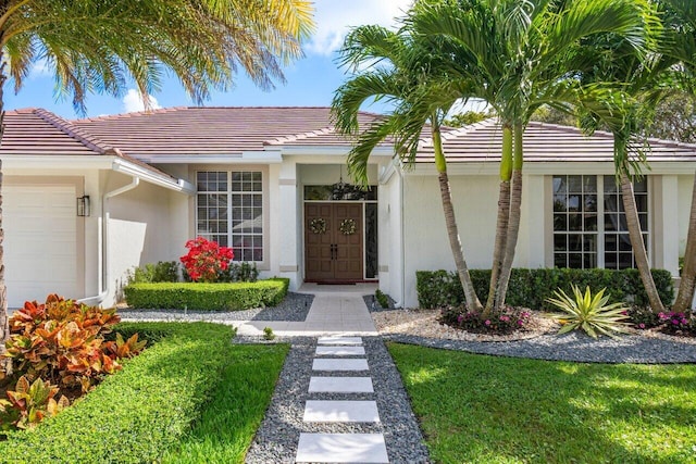 entrance to property with a tile roof, an attached garage, and stucco siding