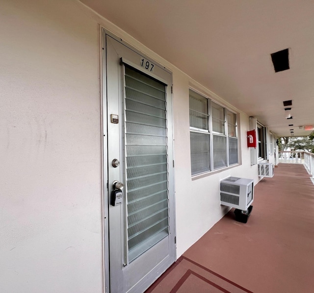 entrance to property featuring covered porch, a wall unit AC, and stucco siding