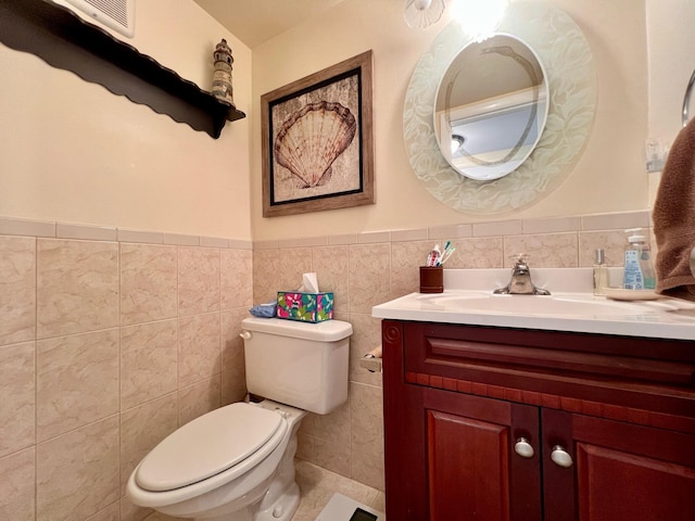 half bath with toilet, a wainscoted wall, tile walls, and vanity