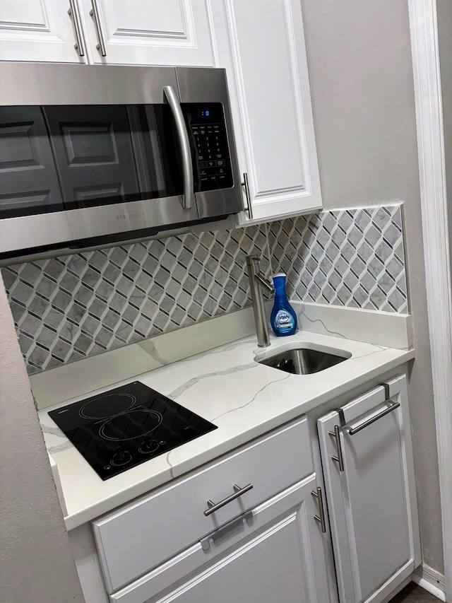 kitchen featuring white cabinetry, light stone countertops, backsplash, and black electric cooktop