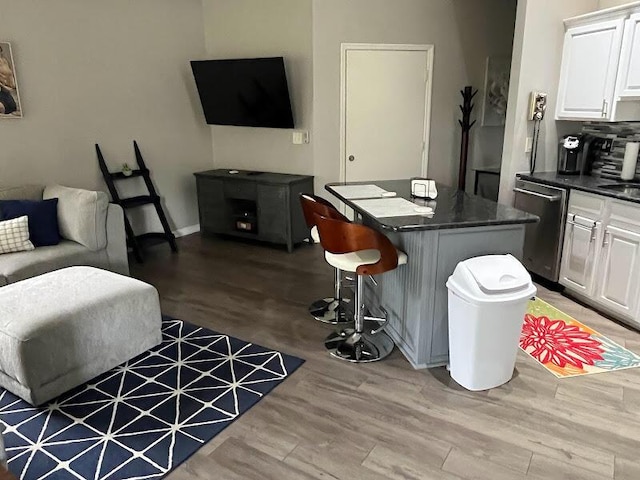 kitchen featuring a kitchen bar, white cabinetry, stainless steel dishwasher, a kitchen island, and hardwood / wood-style floors