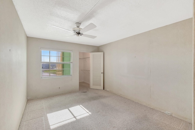 unfurnished bedroom with a walk in closet, light colored carpet, ceiling fan, a textured ceiling, and a closet