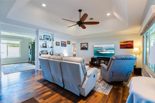 living room featuring crown molding, a tray ceiling, dark wood-type flooring, and ceiling fan