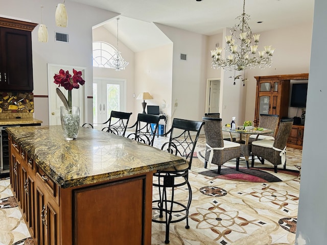 kitchen featuring pendant lighting, high vaulted ceiling, dark stone countertops, a center island, and an inviting chandelier