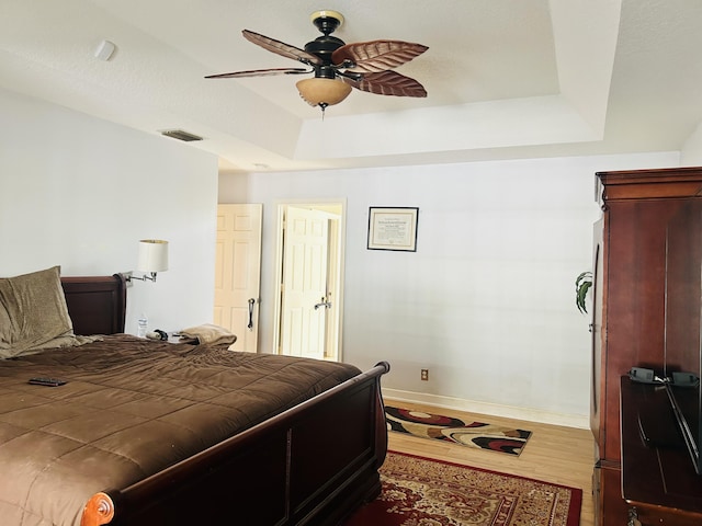 bedroom with hardwood / wood-style flooring, ceiling fan, and a tray ceiling