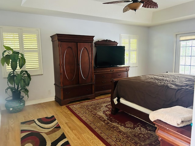 bedroom with ceiling fan, a tray ceiling, and light wood-type flooring