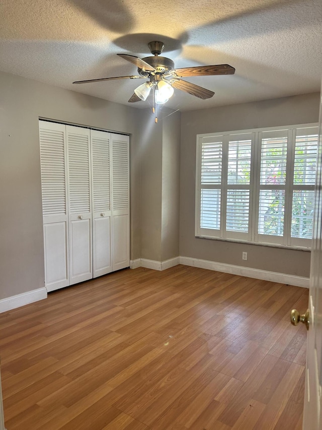 unfurnished bedroom with ceiling fan, a closet, light hardwood / wood-style floors, and a textured ceiling