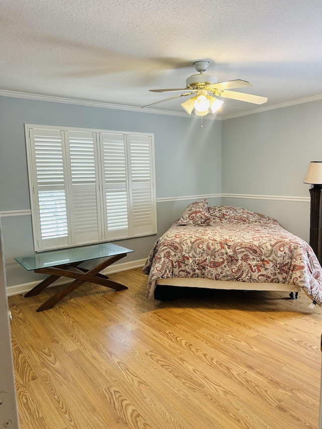 bedroom featuring ceiling fan, ornamental molding, light hardwood / wood-style floors, and a textured ceiling