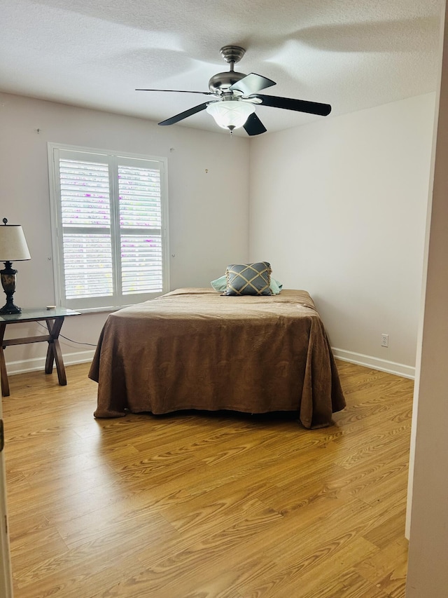 bedroom featuring ceiling fan, light hardwood / wood-style flooring, and a textured ceiling