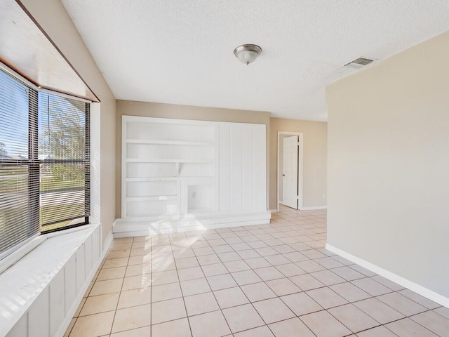 spare room featuring light tile patterned floors, baseboards, visible vents, a textured ceiling, and built in shelves