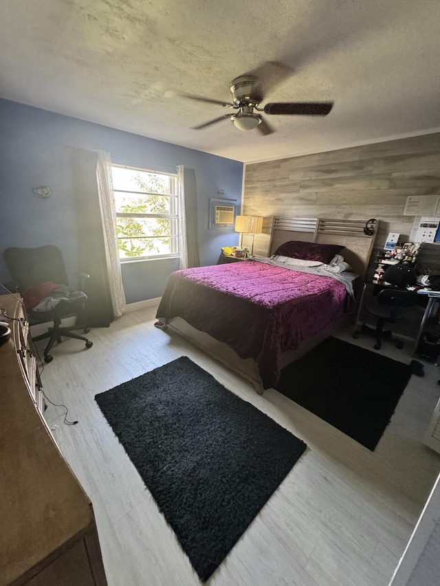 bedroom featuring ceiling fan, wood-type flooring, a textured ceiling, and wooden walls