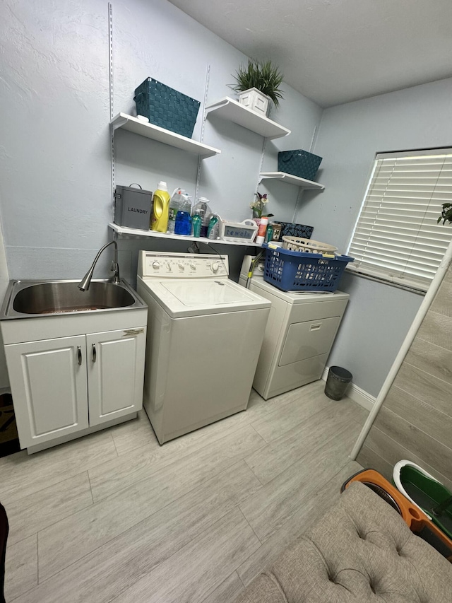 laundry area with cabinets, washing machine and dryer, sink, and light hardwood / wood-style flooring