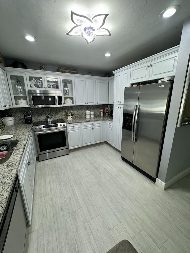 kitchen featuring stainless steel appliances, white cabinetry, light stone countertops, and decorative backsplash