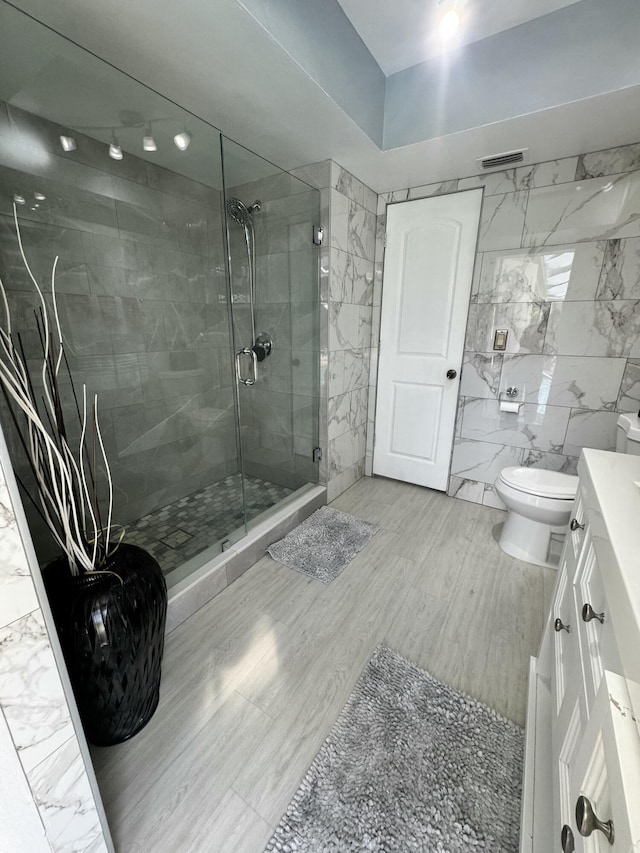 bathroom featuring vanity, a shower with shower door, tile walls, and toilet