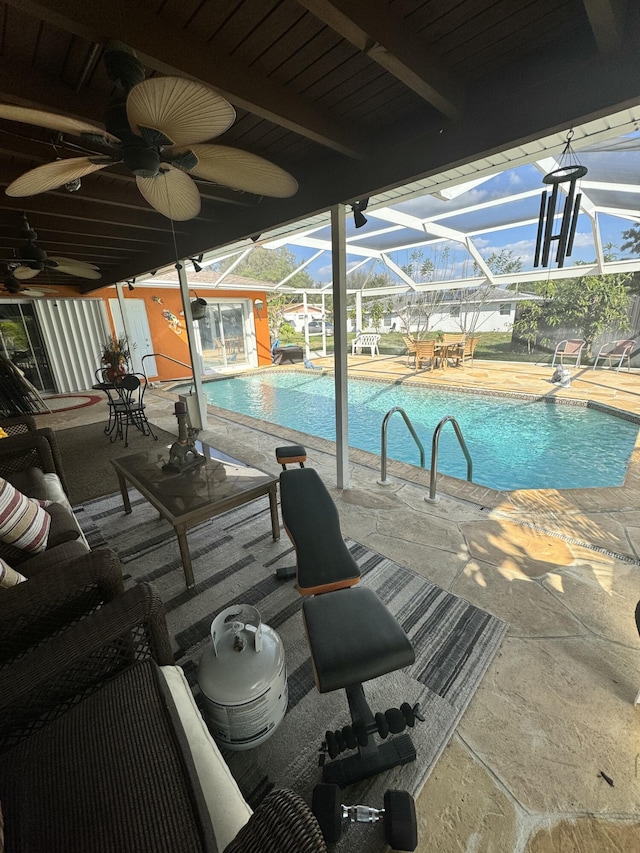 view of swimming pool with ceiling fan, a patio area, glass enclosure, and a storage unit