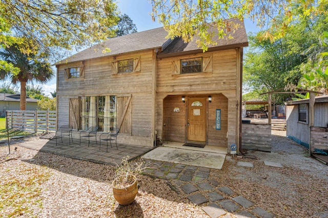 view of front of house with a patio area, fence, and roof with shingles