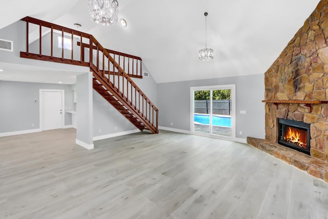 unfurnished living room featuring an inviting chandelier, a fireplace, light hardwood / wood-style flooring, and high vaulted ceiling