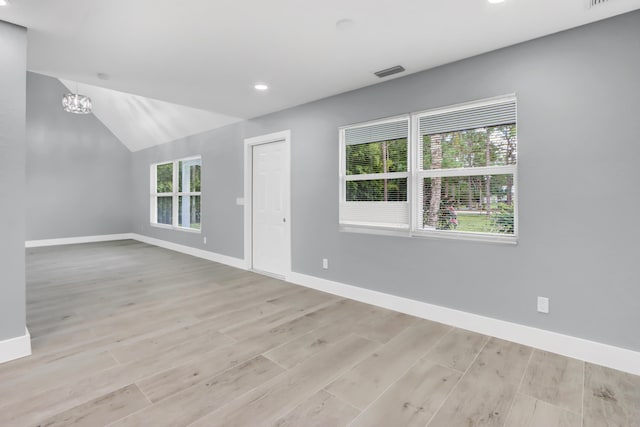 empty room featuring lofted ceiling, a chandelier, and light hardwood / wood-style flooring